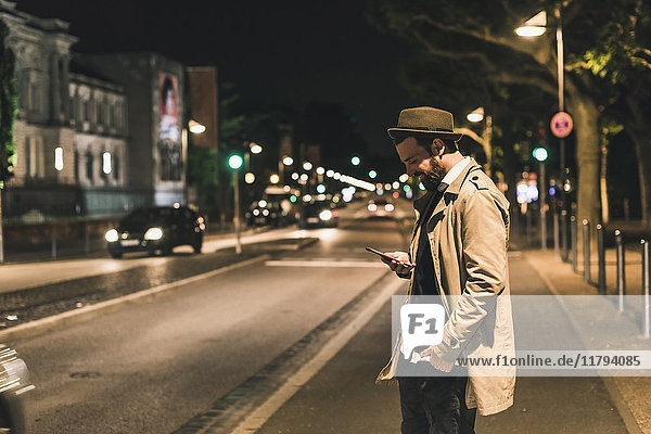 Stylish young man with cell phone on urban street at night