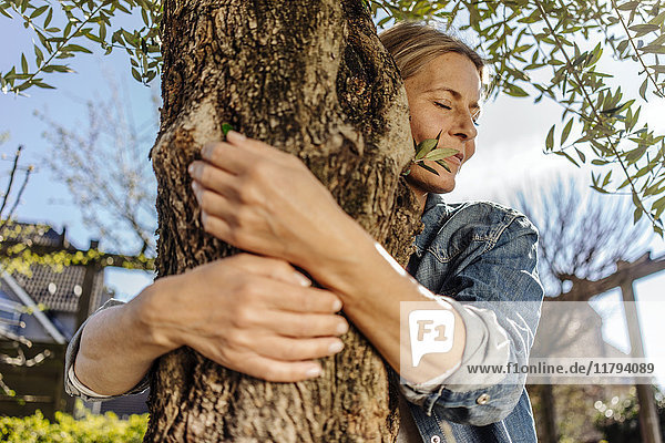 Frau im Garten umarmt einen Baum