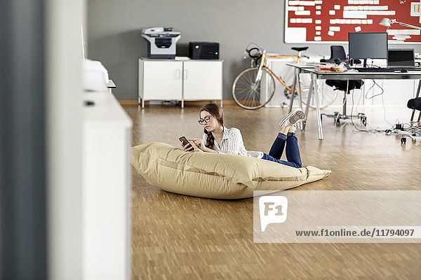 Young woman with cell phone lying in bean bag in office
