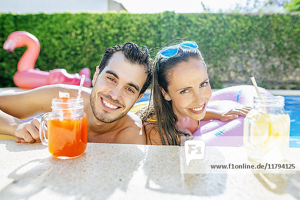 Glückliches Paar im Schwimmbad mit Getränken am Pool