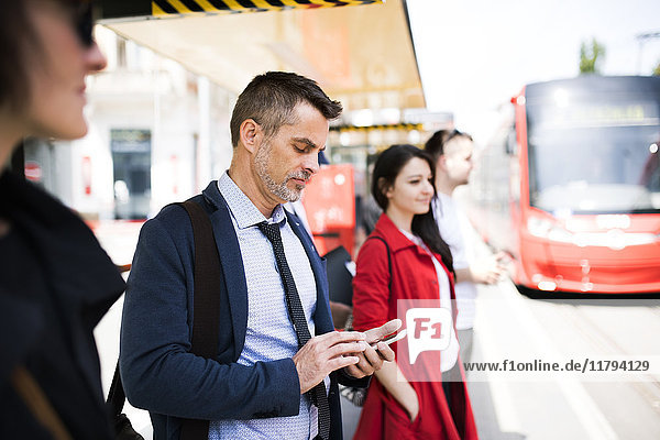 Geschäftsmann mit Smartphone wartet an der Bushaltestelle