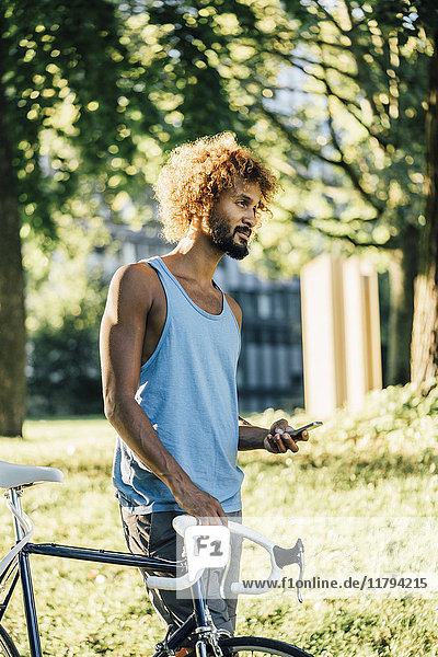 Young man with bicycle and cell phone in park
