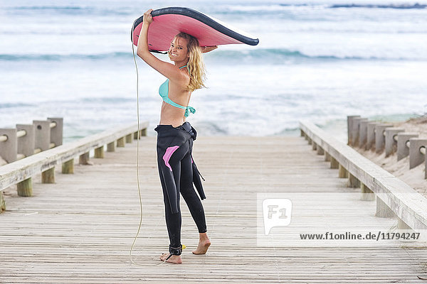 Frau zu Fuß zum Strand mit Surfbrett