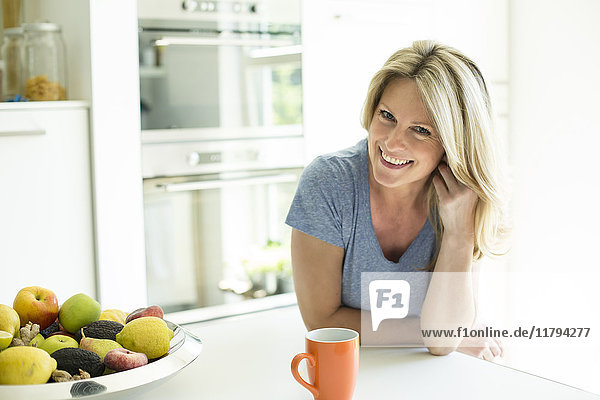 Porträt der lächelnden Frau zu Hause mit Tasse Kaffee und Obstschale