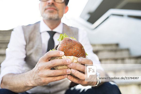 Businessman in the city sitting on stairs eating a hamburger