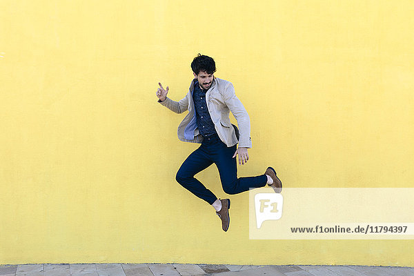 Junger Mann springt in die Luft vor der gelben Wand