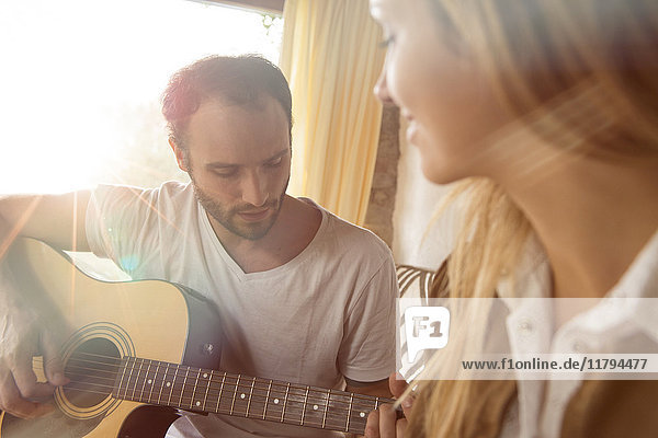 Mann  der zu Hause Gitarre spielt  während seine Freundin ihn beobachtet.