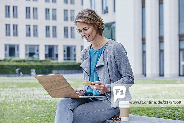 Woman outdoors with laptop  credit card and takeaway coffee