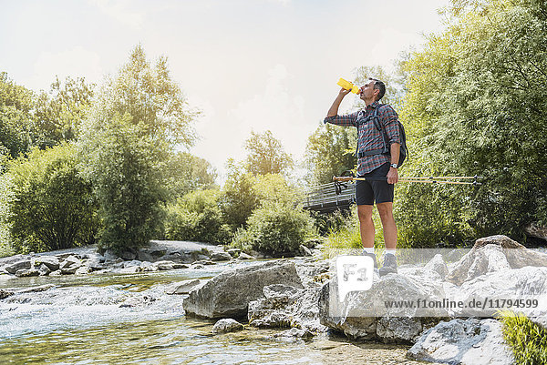 Hiker standing at the riverbank drinking from bottle