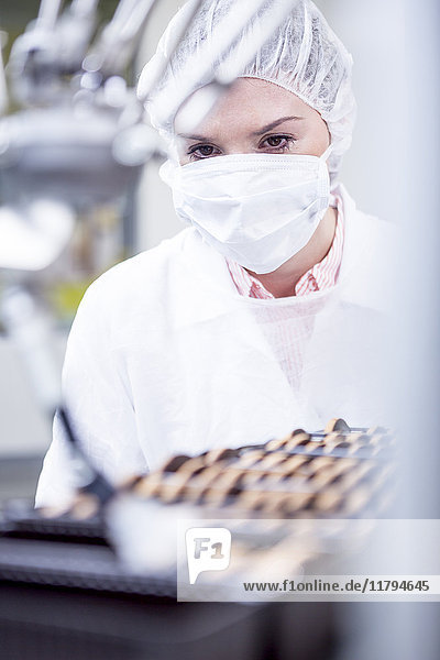 Frau in der Fabrik schaut sich den Roboter an  der Kekse handhabt