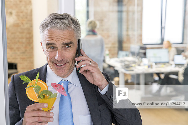 Ein reifer Geschäftsmann trinkt einen Cocktail,  während er telefoniert.