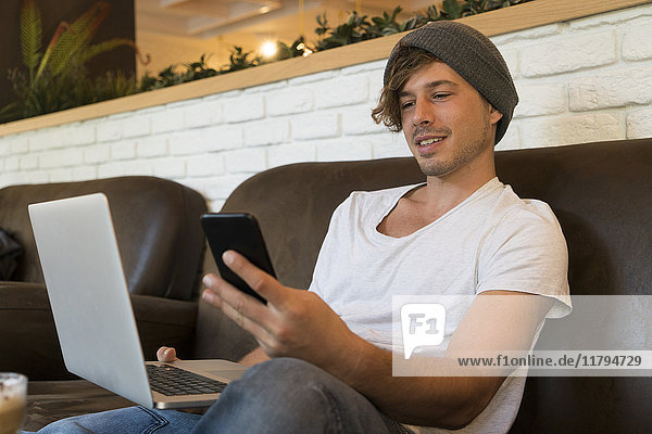 Young man using cell phone and laptop in a cafe