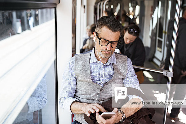 Businessman with smartphone and earphones travelling in tram