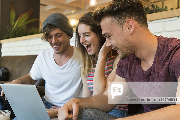 Drei aufgeregte Freunde betrachten Laptop in einem Café