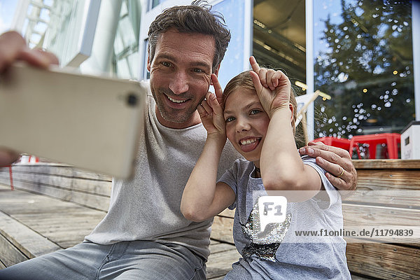 Father and playful daughter taking a selfie at an outdoor cafe