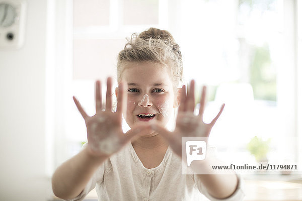 Porträt des lächelnden Mädchens in der Küche mit Teig auf Händen und Gesicht