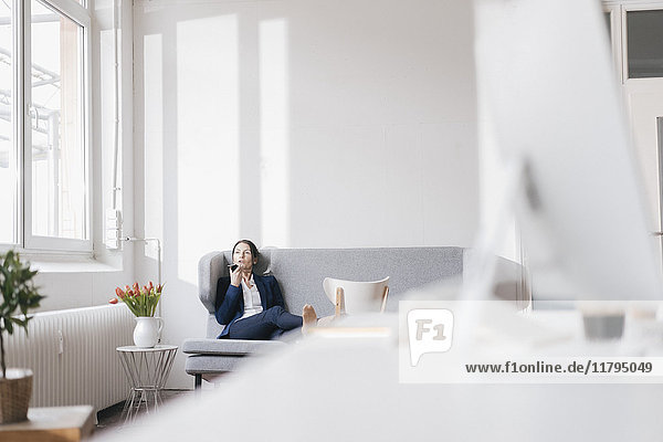 Businesswoman sitting on couch in a loft using cell phone