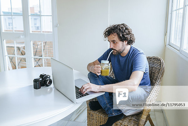 Mann trinkt Gemüsesaft  während er den Laptop zu Hause benutzt.
