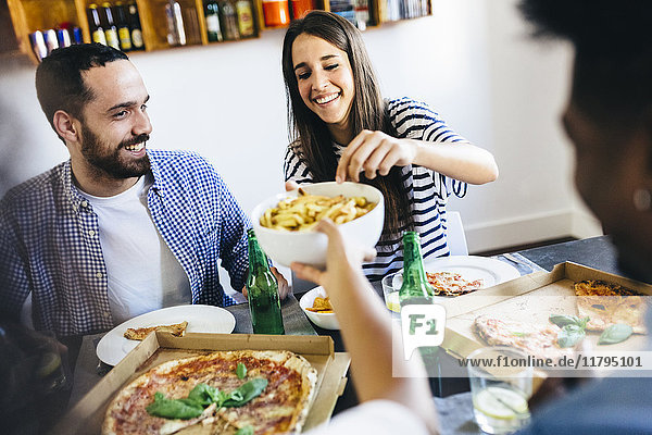 Happy friends having French fries and pizza at home