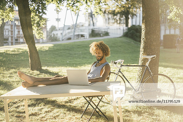Man with beard and curly hair using laptop at table in park