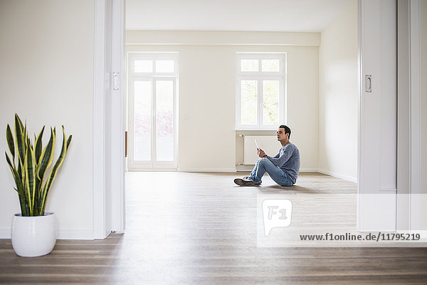Junger Mann im neuen Zuhause sitzend auf dem Boden mit Tablette