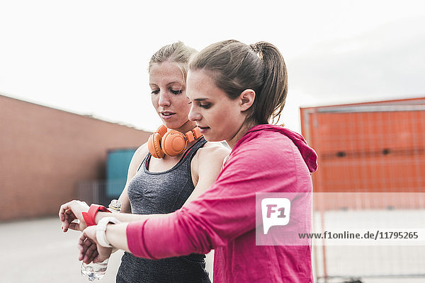 Zwei Frauen  die eine Pause vom Sport machen und auf ihre Smartuhren schauen.