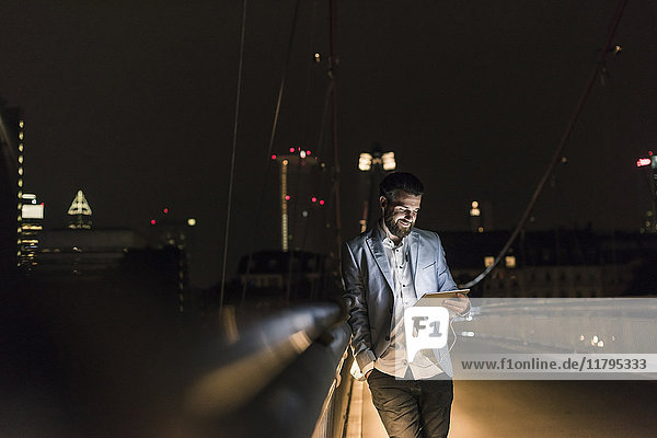 Junger Mann mit Tablett und Kopfhörer auf Stadtbrücke bei Nacht