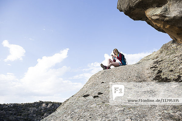Spain  Madrid  young woman resting on a rock using her phone during a trekking day