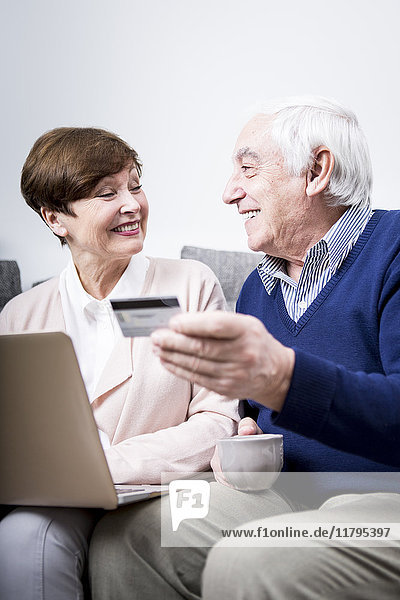 Senior couple lying on couch doing online shopping with credit card