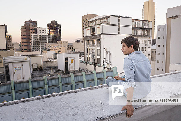 Young man sitting on balustrade of a rooftop terrace  looking at view