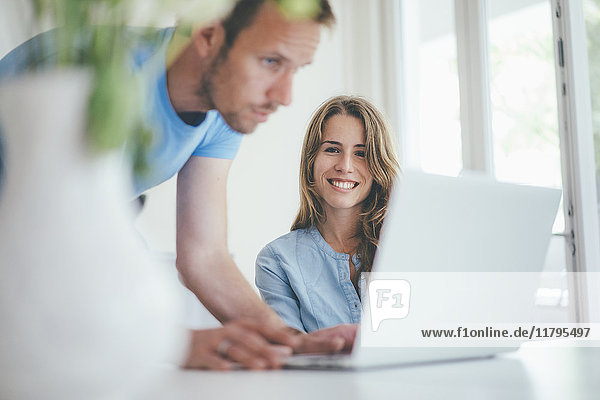 Smiling young woman and man using laptop at home