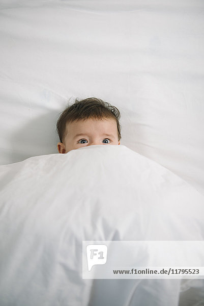 Portrait of scared baby girl lying under white blanket