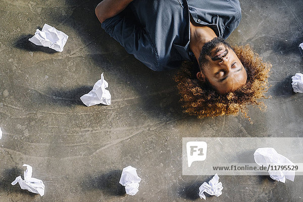 Man lying on the floor surrounded by crumpled paper