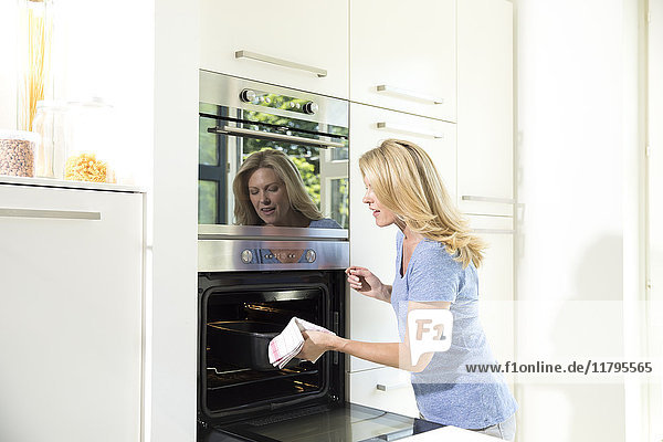 Frau in der Küche nimmt Auflaufform aus dem Ofen