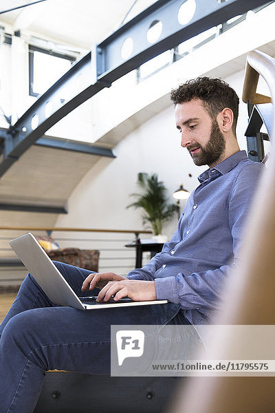 Mann auf dem Boden sitzend mit Laptop im modernen Büro