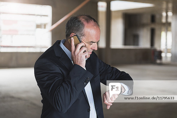 Businessman on cell phone in building under construction checking the time