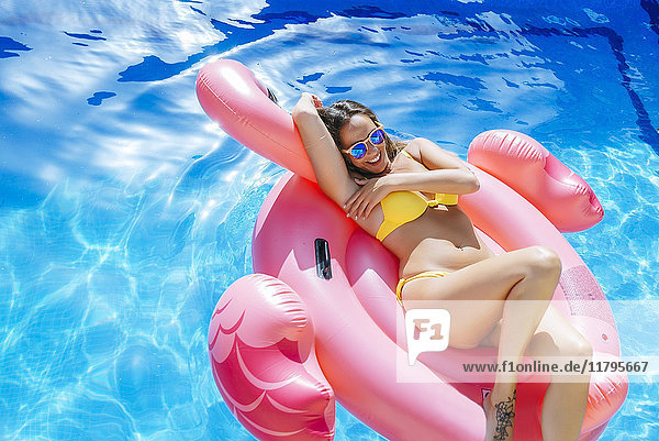 Sorglose junge Frau auf rosa Flamingoschwimmer im Schwimmbad