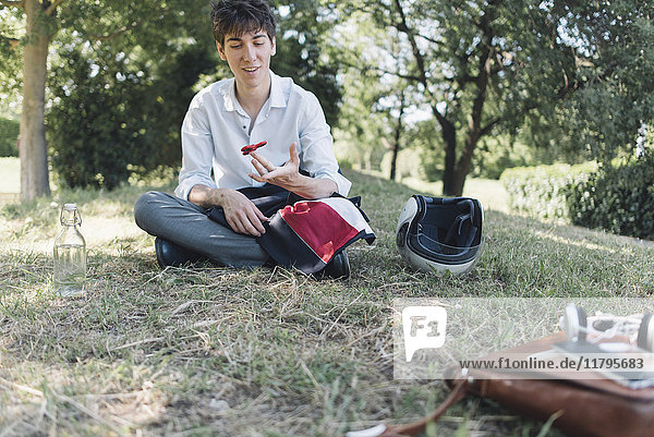 Young man sitting on meadow in park using a fidget spinner