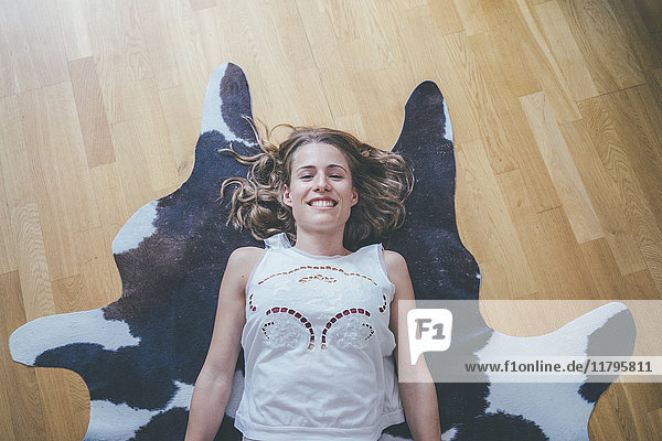 Porträt einer lächelnden jungen Frau  die auf einem Pelz auf dem Boden liegt