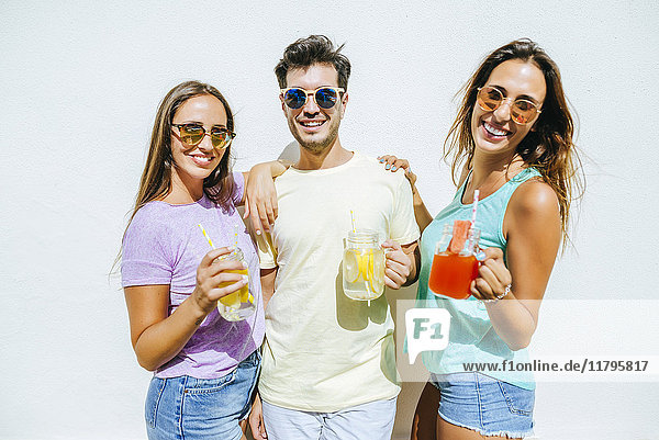 Happy friends holding refreshing drinks in front of white wall