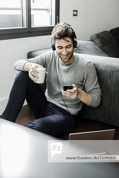 Lächelnder junger Mann mit Handy  Laptop und Kopfhörer zu Hause