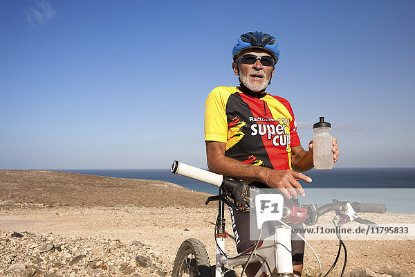 Spanien  Kanarische Inseln  Fuerteventura  älterer Mann mit Mountainbike beim Ausruhen