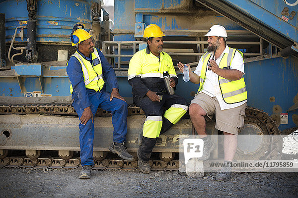 Colleague workers at quarry sitting on machine  taking a break