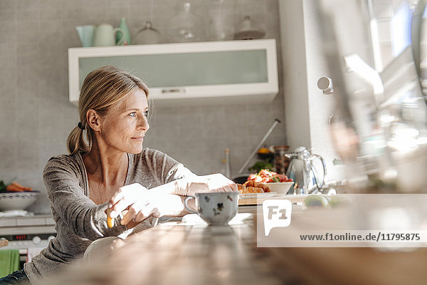 Woman at home in kitchen looking out of window