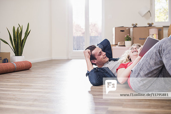 Glückliches junges Paar in neuem Zuhause auf dem Boden liegend mit Tablette