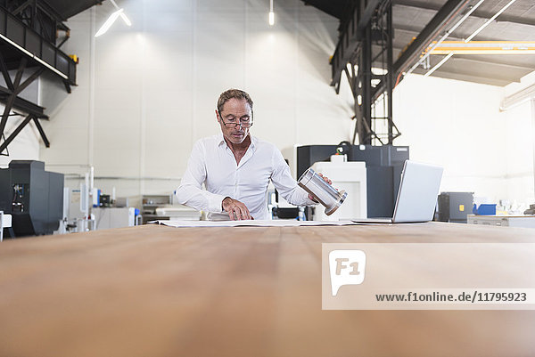 Mann mit Plan  Produkt und Laptop auf dem Tisch in der Fabrik