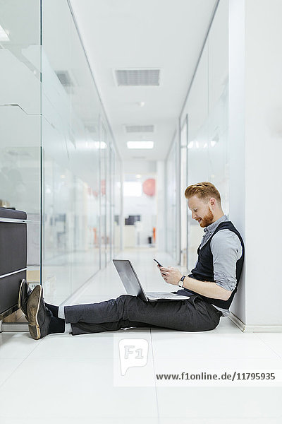 Geschäftsmann im Büro sitzend auf dem Boden  mit Laptop