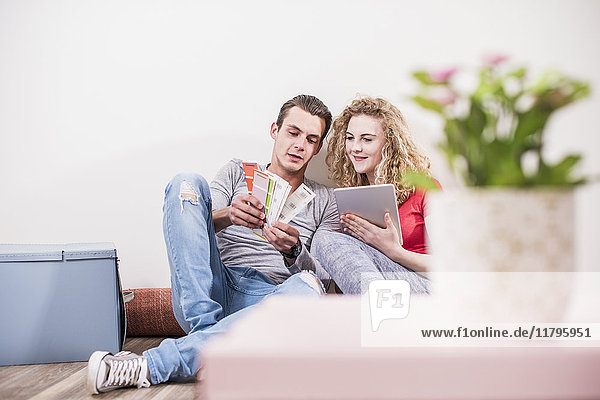 Young couple in new home sitting on floor with tablet choosing from color sample