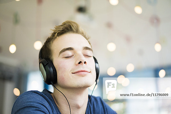 Porträt eines lächelnden jungen Mannes mit geschlossenen Augen Musik hören mit Kopfhörer