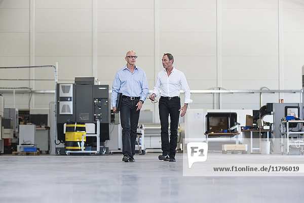 Two businessmen walking and talking in factory shop floor
